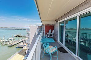 Un balcon avec vue sur l’eau, une table et des chaises, et une porte donnant sur un espace abrité.