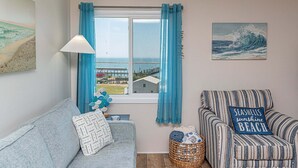 Ett rum med utsikt över havet, en soffa, en randig fåtölj, en lampa och en tavla.