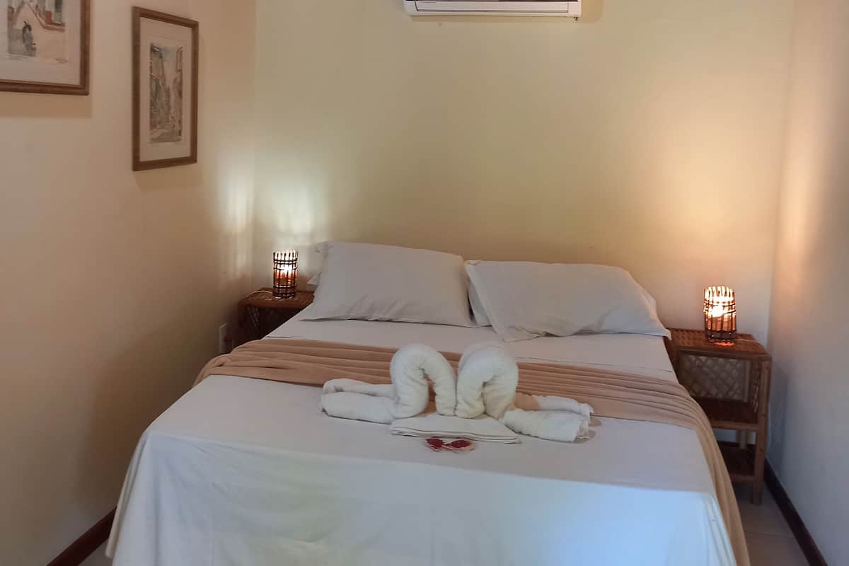 A neatly made bed with white linens and towels, a wooden ceiling, and a wall-mounted air conditioner.