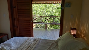 A room with a bed, a wooden door leading to an outdoor deck, and a small table. - Pousada Cais Dourado (Maraú)