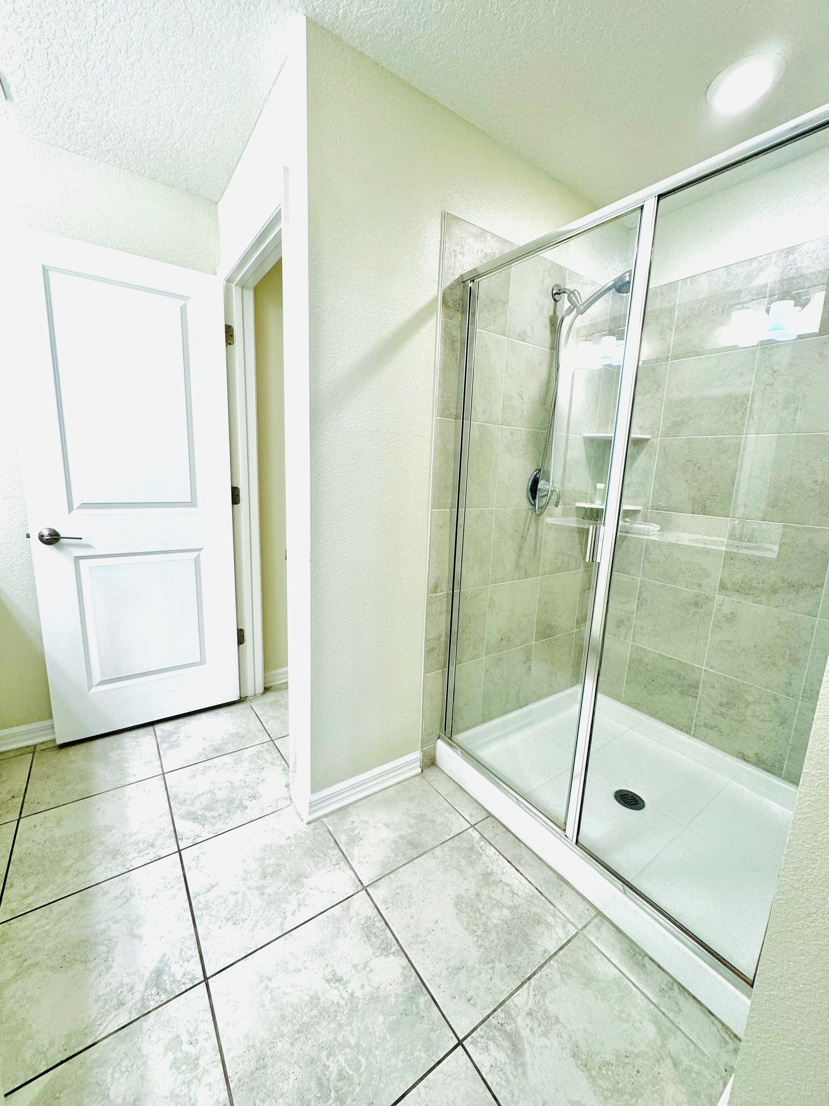 Un baño con cabina de ducha de vidrio, suelo de baldosas y puerta blanca.