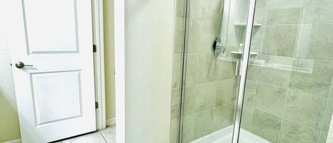 Un baño con cabina de ducha de vidrio, suelo de baldosas y puerta blanca.