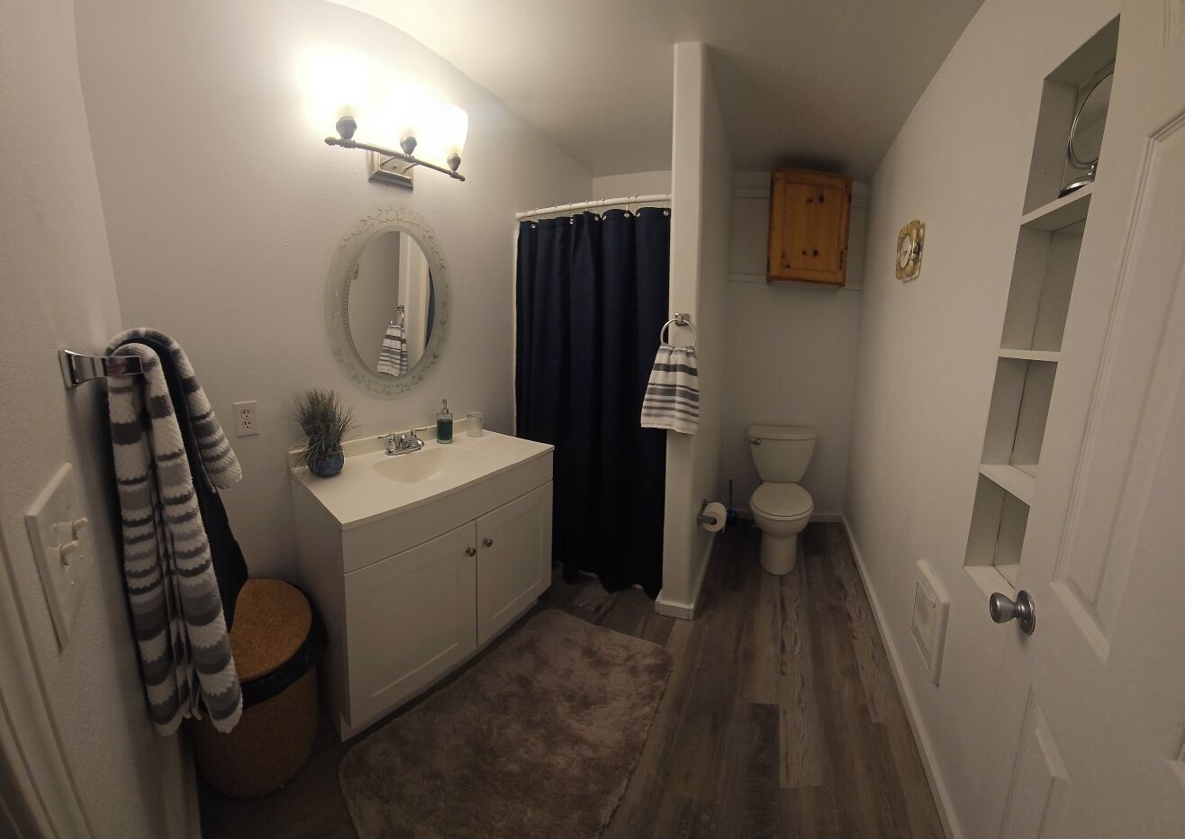 Une salle de bain avec un meuble-lavabo blanc, un miroir rond, des toilettes et un rideau de douche.