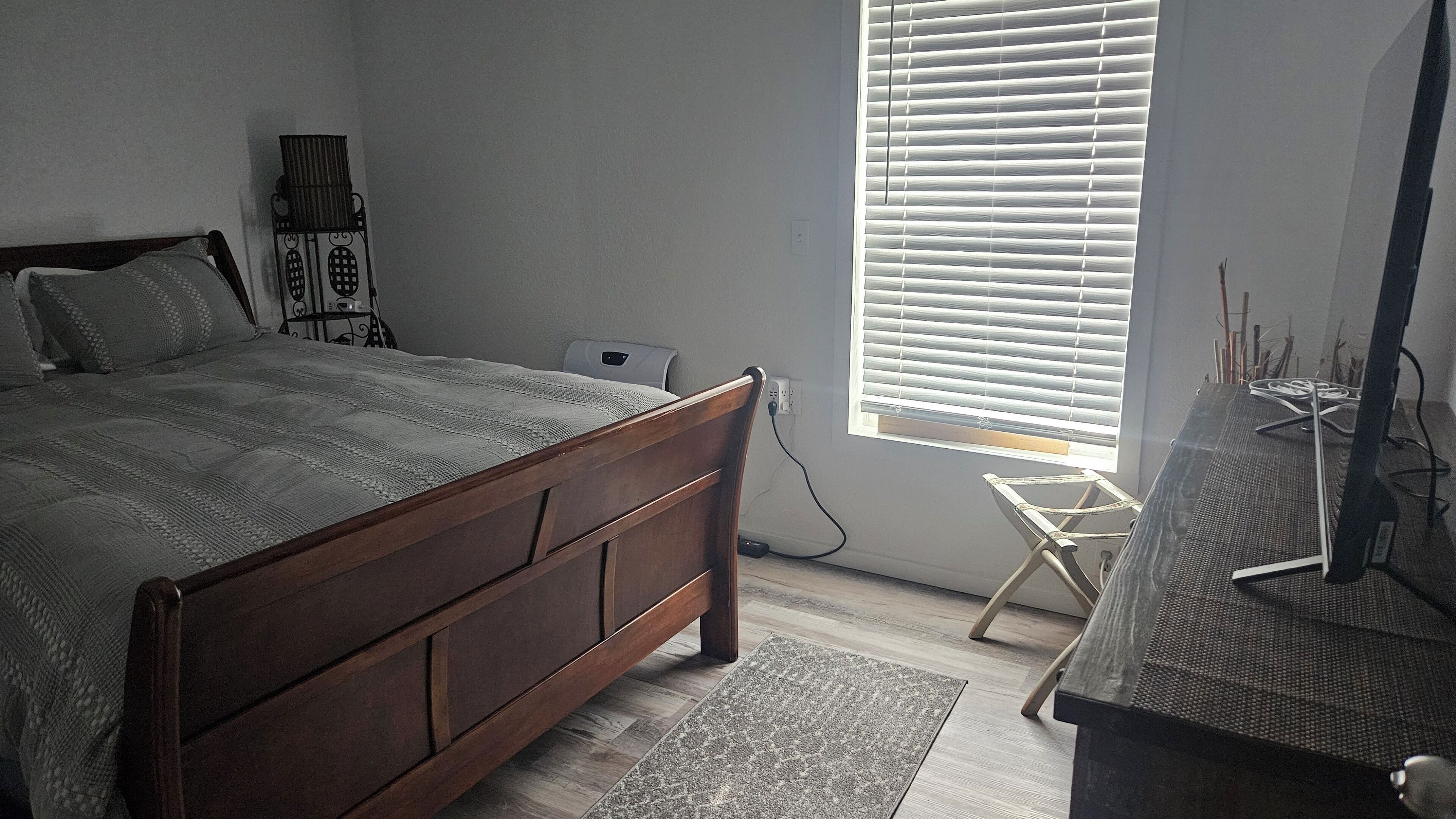 A bedroom with a wooden bed, a desk with a computer, and a window with blinds.