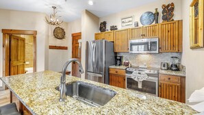 A kitchen with granite countertops, stainless steel appliances, wooden cabinets, and a chandelier. - Mountain Thunder Bluebird Condo: Ski In, Top-Floor w/ Views, Resort Amenities (Breckenridge)