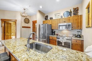 A kitchen with granite countertops, stainless steel appliances, wooden cabinets, and a chandelier.