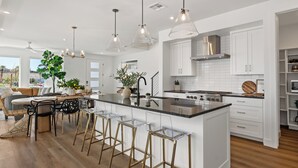 A modern kitchen with white cabinets, a central island with stools, pendant lighting, and a view of the outdoors. - The Sapphire Blanc: Desert Color Lagoon + Beaches (St. George)