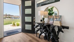A modern entryway with a black door, a wooden console table, a mirror, and a painting of a beach scene. - The Sapphire Blanc: Desert Color Lagoon + Beaches (St. George)