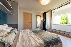 Ein modernes Schlafzimmer mit einem großen Bett, einem Kleiderschrank und einer Glastür, die auf einen Balkon führt.