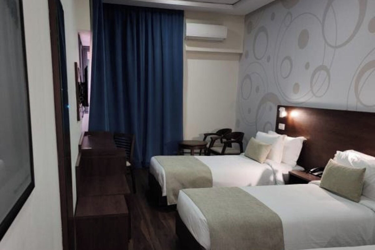 Quarto de hotel com duas camas, uma mesa e uma cadeira.