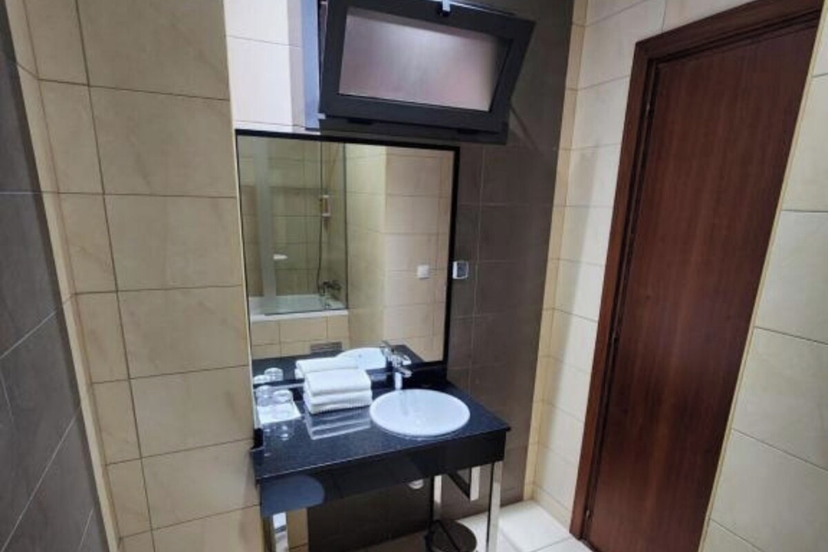 A small bathroom with a toilet, sink, mirror, and a television mounted above the sink.