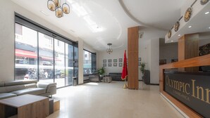 Eine moderne Hotelhalle mit Empfangstresen, Sitzgelegenheiten und großen Fenstern mit Blick auf die Straße.