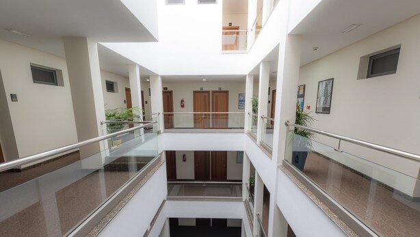 Ein mehrgeschossiges Interieur mit Glasgeländern, einer zentralen Treppe und Holztüren.