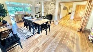 A spacious living room with a wooden floor, a dining area with a wooden table and chairs, a fireplace, and a view of the outdoors. - Spacious Stylish Forest Escape | Kids Outdoor Play (Saint Leonards)