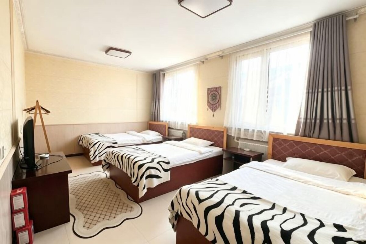 Hotellihuone, jossa on kolme sänkyä, työpöytä, tuoli ja televisio.