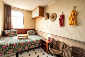 Une pièce de taille modeste, comprenant un lit, une petite table, une chaise et une fenêtre avec des rideaux.