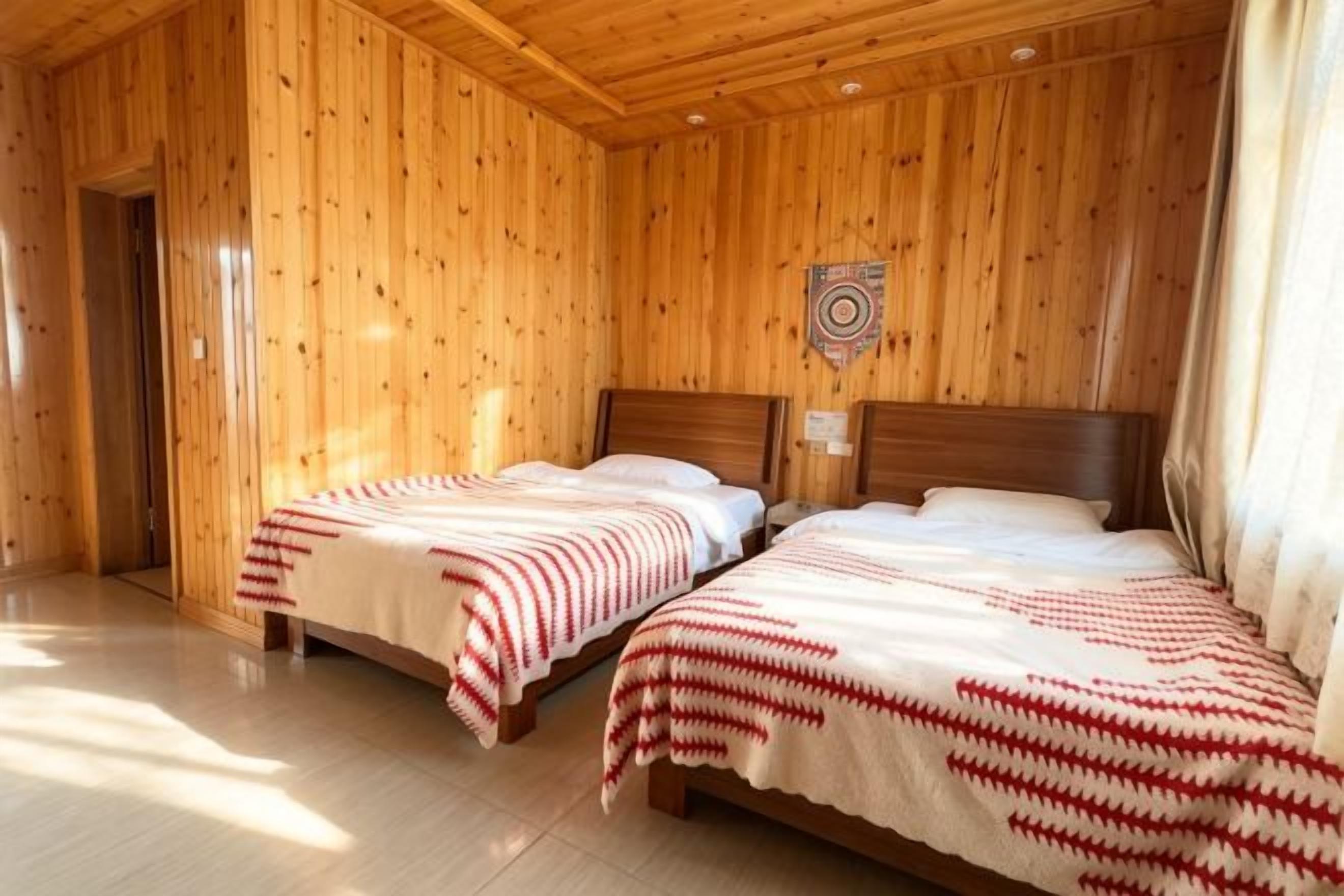 Una habitación con dos camas de madera, techo de madera y un blanco en la pared.