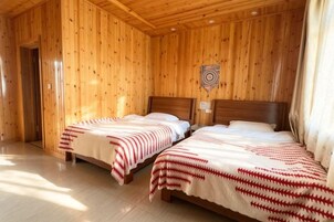 Una habitación con dos camas de madera, techo de madera y un blanco en la pared.