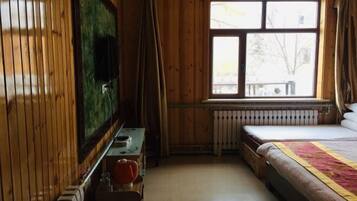 Une pièce aux murs lambrissés, comprenant un lit, un radiateur, une fenêtre et un téléviseur.