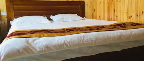 A neatly made bed with white linens and a decorative blanket in a room with wooden paneling.