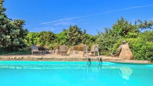 Una piscina con sillones de madera y una escultura de piedra.