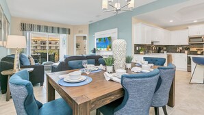 A modern kitchen with white cabinets, a microwave, and a dining area with a wooden table and blue chairs. - Luxury Condo 5mi to Disney with FREE water park access! (Kissimmee)