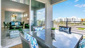 A modern balcony with a glass table, green chairs, and a sofa with patterned cushions. - Luxury Condo 5mi to Disney with FREE water park access! (Kissimmee)