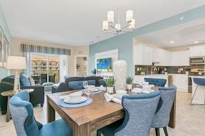 Un espace repas moderne avec une table en bois dressée pour quatre personnes, entourée de chaises à l’assise rembourrée de tissu bleu.