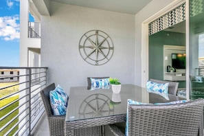 Un balcon avec une table en verre, des chaises en osier et une boussole fixée au mur.