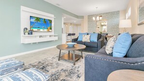 A living room with a flat-screen TV, a sofa, a coffee table, and a dining area in the background. - Luxury Condo 5mi to Disney with FREE water park access! (Kissimmee)