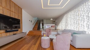A modern living room with a wooden floor, a flat-screen TV mounted on a wall, a staircase leading to an upper level, and a patterned wall. - Villa Calla ZadarVillas (Petrcane)