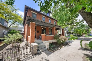 A two-story brick house with a front porch, a small garden, and a metal fence. - 3BR Home  with Private Patio in the German Village (Columbus)