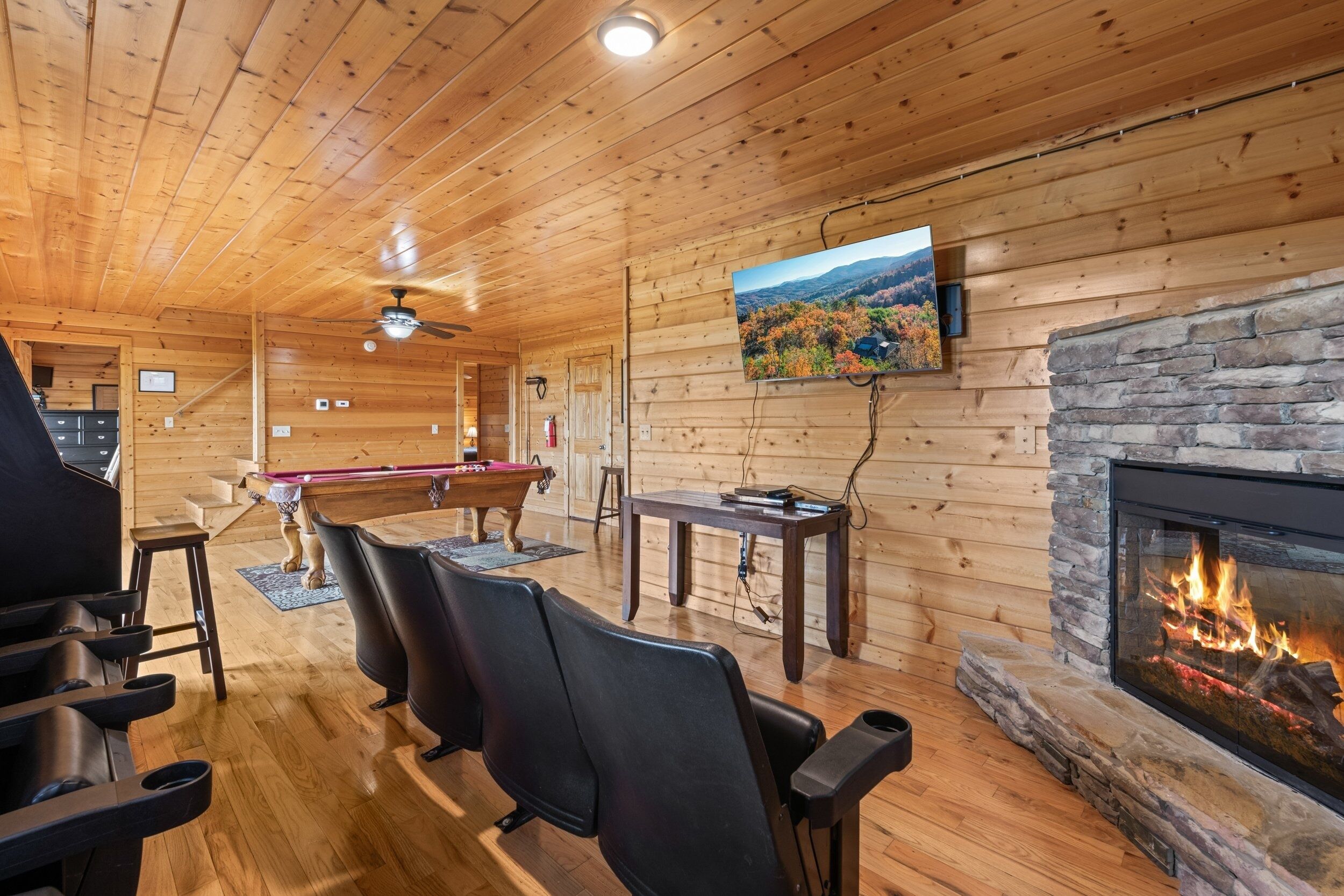 A cozy cabin interior with a fireplace, wooden walls, a pool table, and comfortable seating.