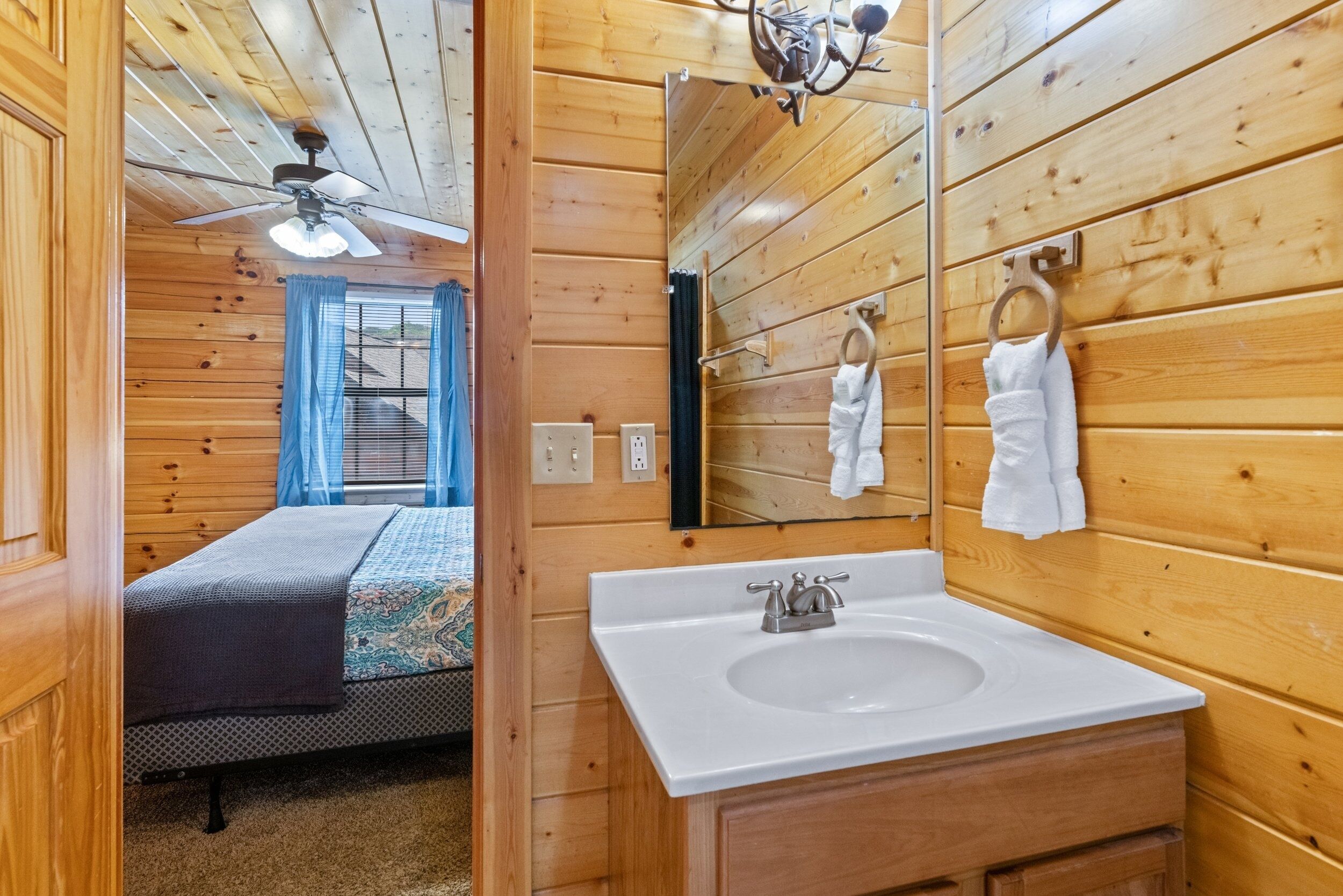 Une pièce de style cabane en bois, avec un lit, un lavabo blanc et un ventilateur de plafond.