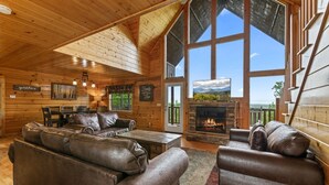 A cozy cabin interior with a large wooden ceiling, a fireplace, leather sofas, and a dining area. - Panoramic View 6 Bedroom Cabin by RedAwning (Sevierville)
