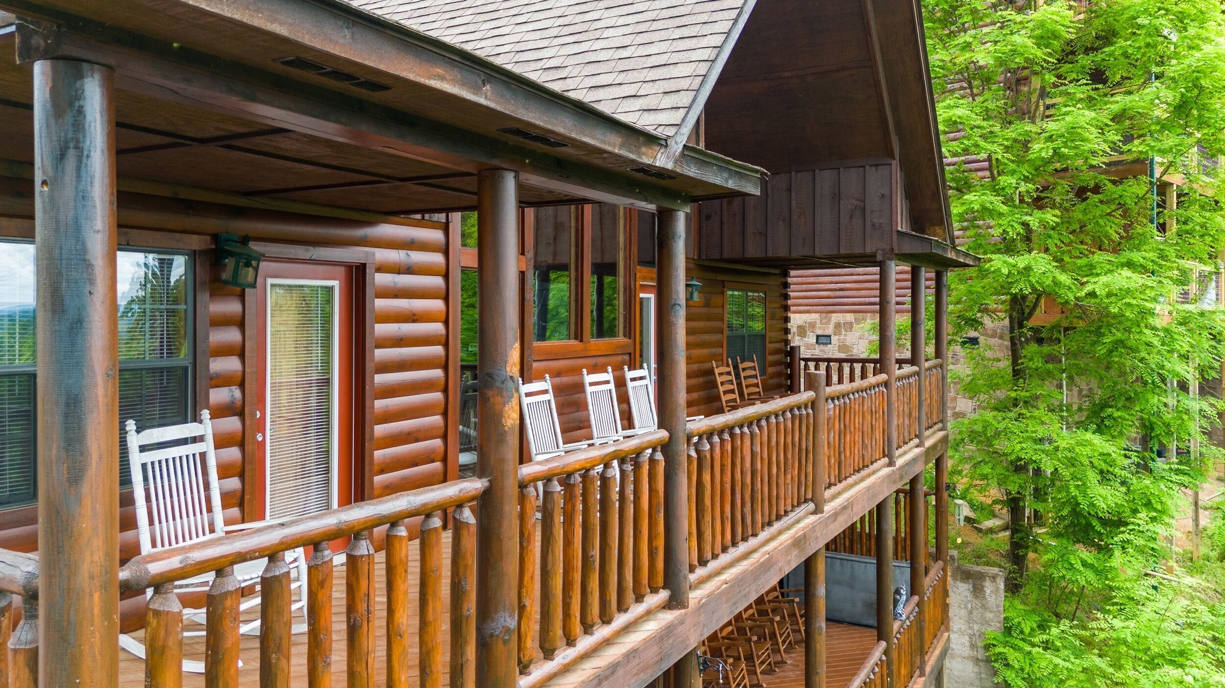 A wooden log cabin with a balcony, large windows, and a stone wall.