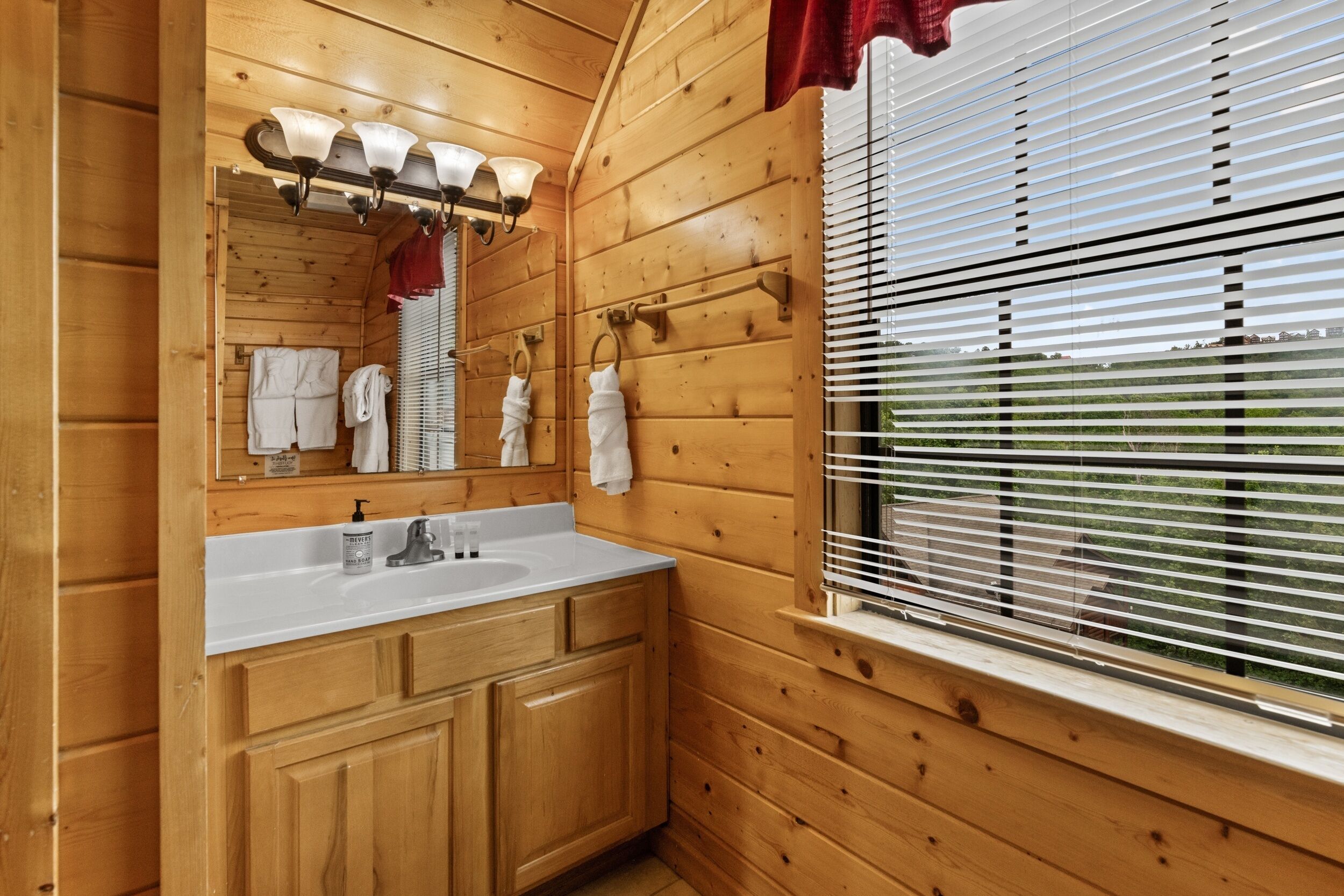 A wooden cabin bathroom with a sink, mirror, and window with blinds.
