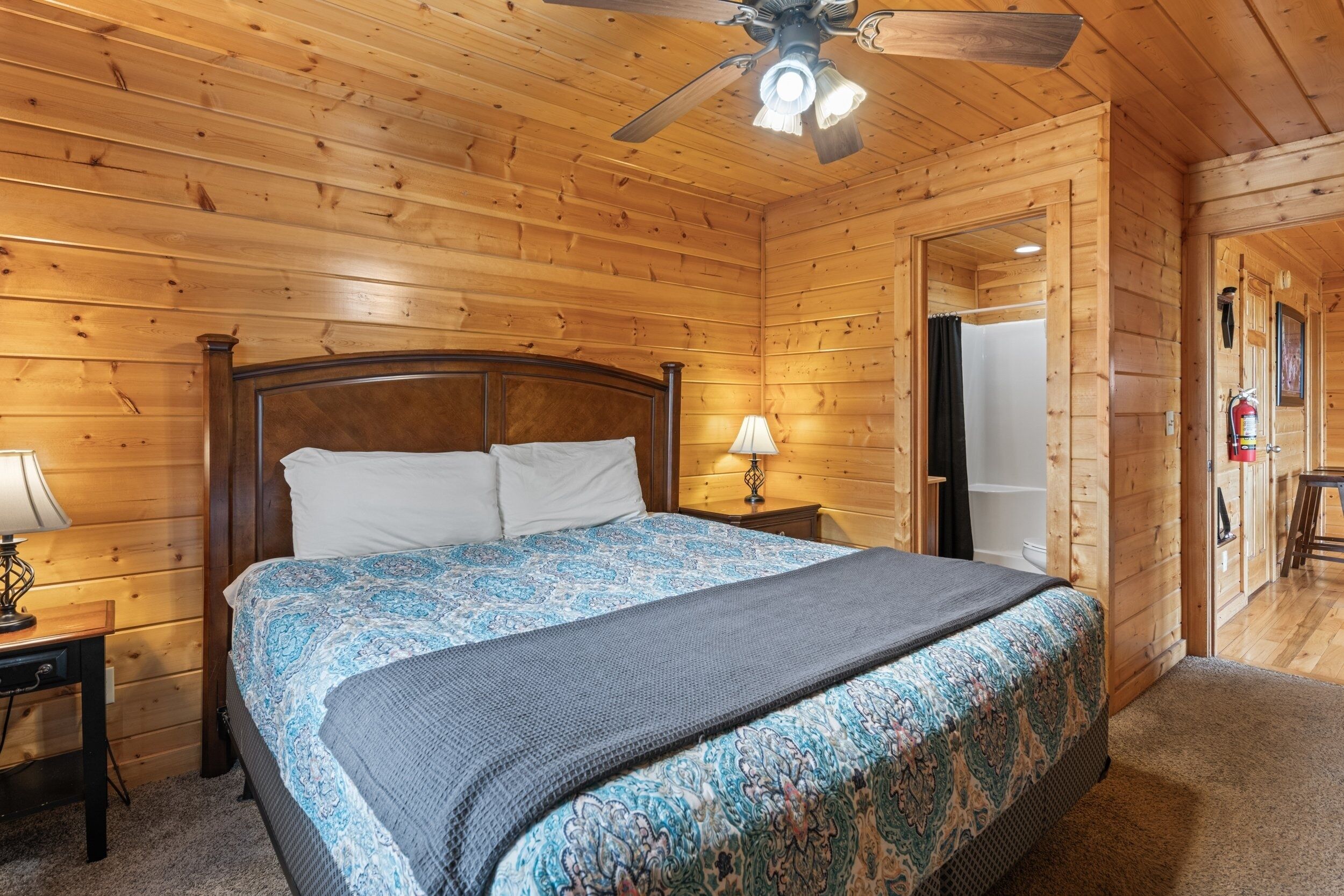 A wooden cabin bedroom with a bed, nightstand, lamp, and ceiling fan.