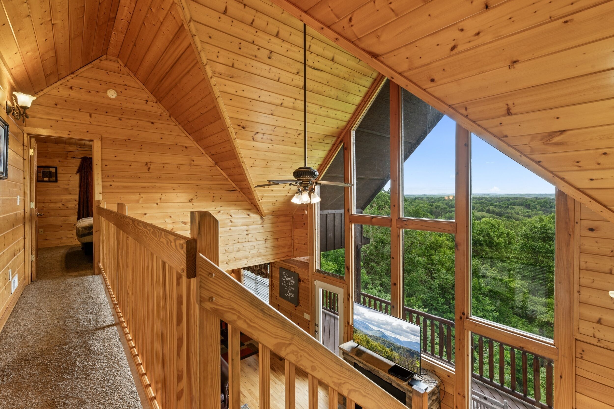 A wooden interior with a high ceiling, a staircase, and large windows offering a view of a forest.