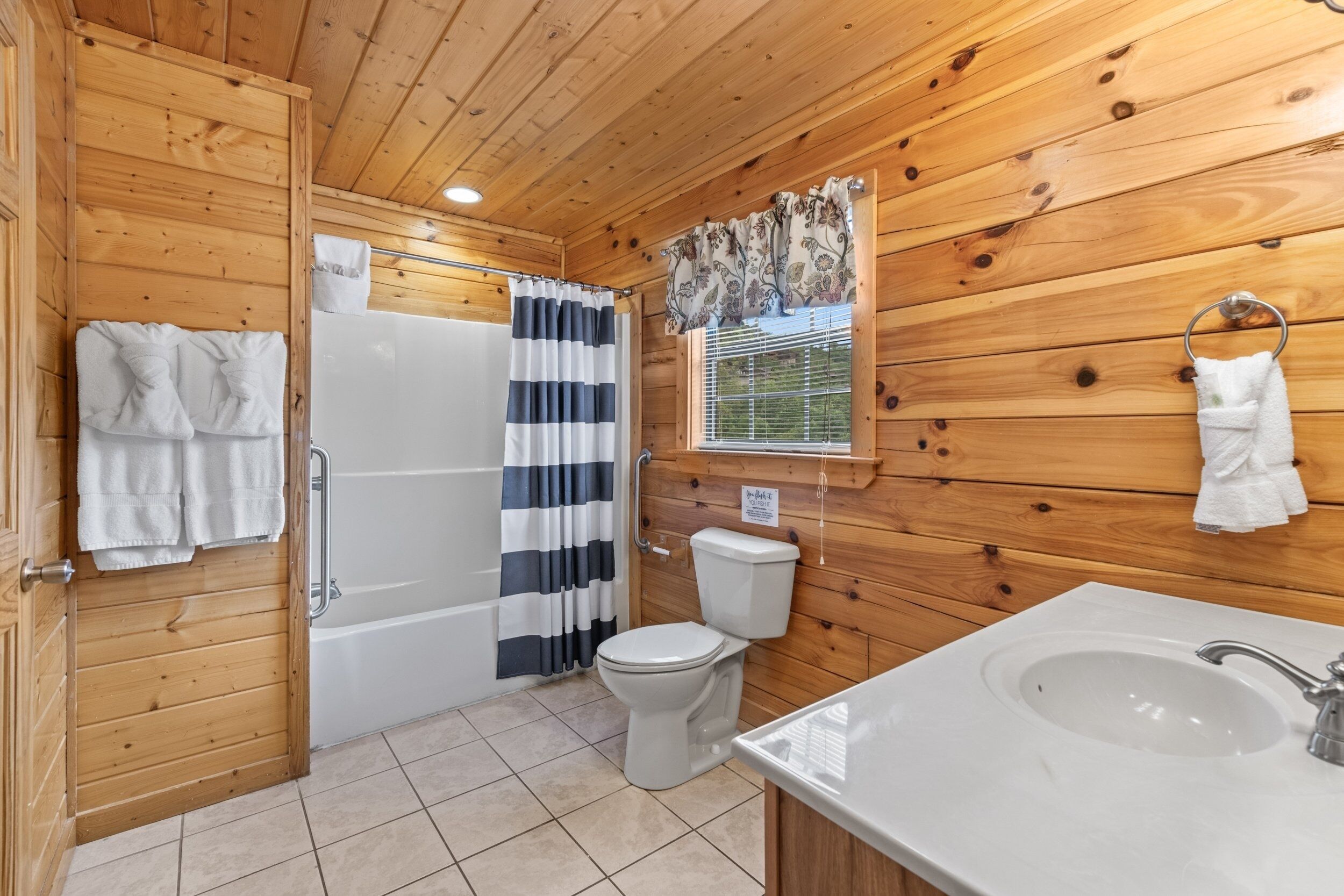 A wooden-paneled bathroom with a white sink, toilet, and shower.