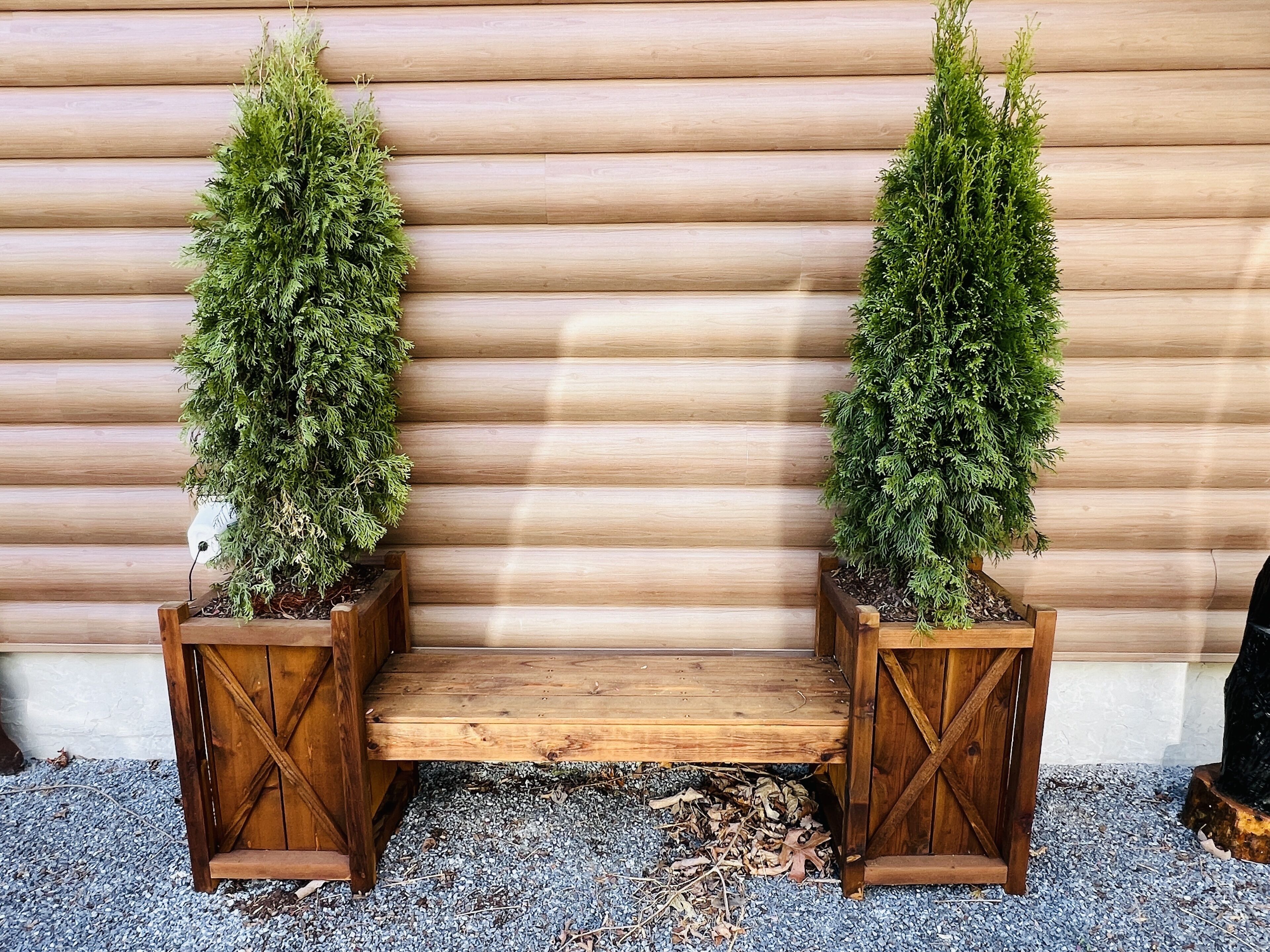 Two wooden planters with green plants against a wooden wall.