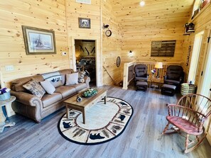 L’intérieur d’un chalet accueillant, avec un canapé en cuir marron, une table basse en bois, un fauteuil à bascule et une cheminée.