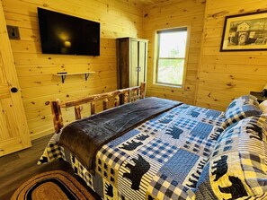 Une chambre dans une cabane en bois, avec un lit, un téléviseur fixé au mur, une fenêtre et une porte.
