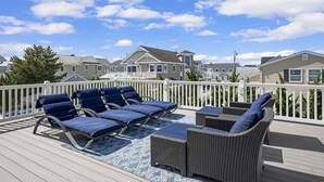 A deck with wicker furniture and a blue rug, overlooking a row of houses. - Seaside Serenity - Stone Harbor, NJ (Stone Harbor)