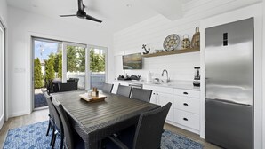 A modern kitchen with a large refrigerator, a dining area with wicker furniture, and a sliding glass door leading to an outdoor patio. - Seaside Serenity - Stone Harbor, NJ (Stone Harbor)