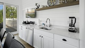 A modern kitchen with white cabinetry, a stainless steel sink, a built-in stove, and a large window overlooking a deck. - Seaside Serenity - Stone Harbor, NJ (Stone Harbor)
