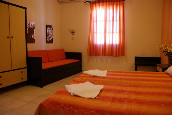 A bedroom with a bed, a sofa, a wardrobe, and a window with curtains. - Verykokkos on the Beach (Naxos)