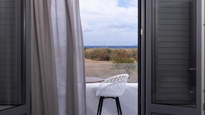 Ein Balkon mit weißem Stuhl, Blick auf das Meer und einem Holzbalken über dem Fenster.