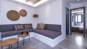 Ein modernes Wohnzimmer mit einem grauen Ecksofa, zwei kleinen runden Tischen und einer gewebten Wanddekoration.