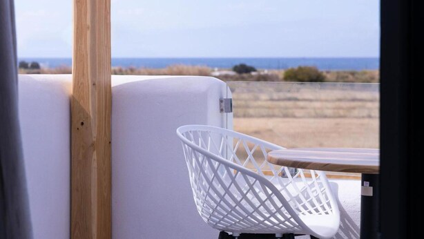 Ein weißer Stuhl mit einem Holztisch, eine weiße Wand und Blick aufs Meer.